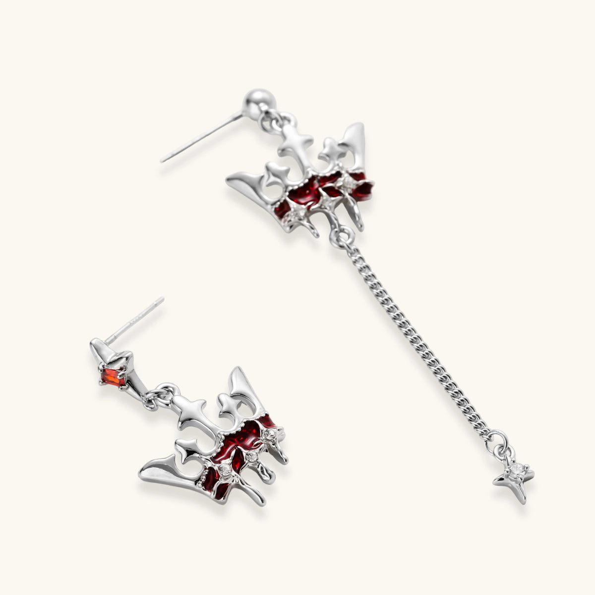 Silver-tone crown pendant with red zirconia stones and matching asymmetrical earrings on cream background