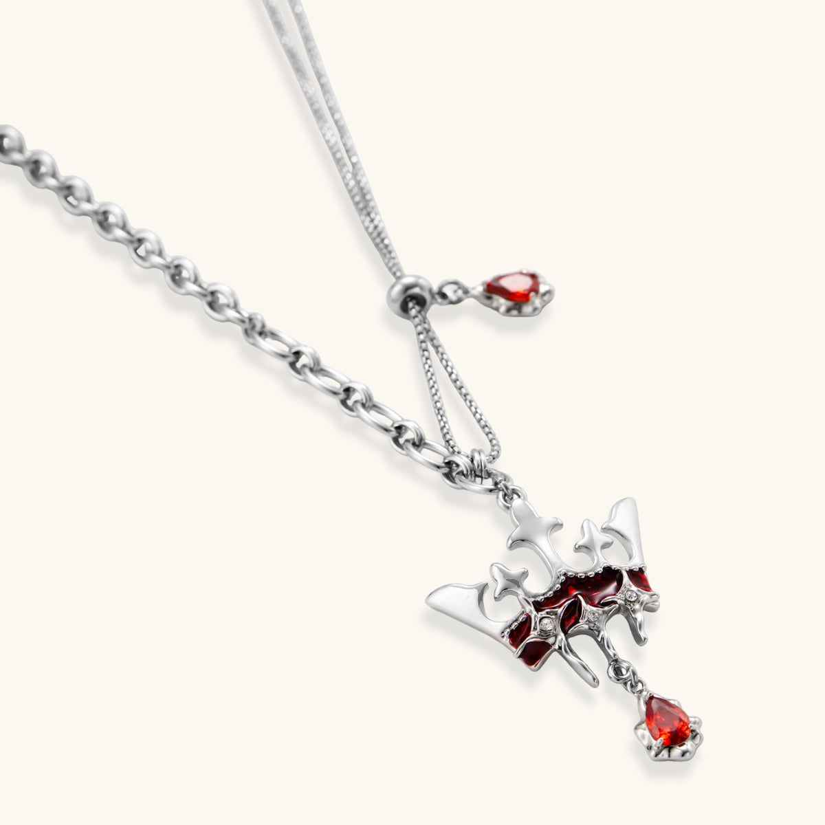 Silver-tone crown pendant with red zirconia stones and matching asymmetrical earrings on cream background