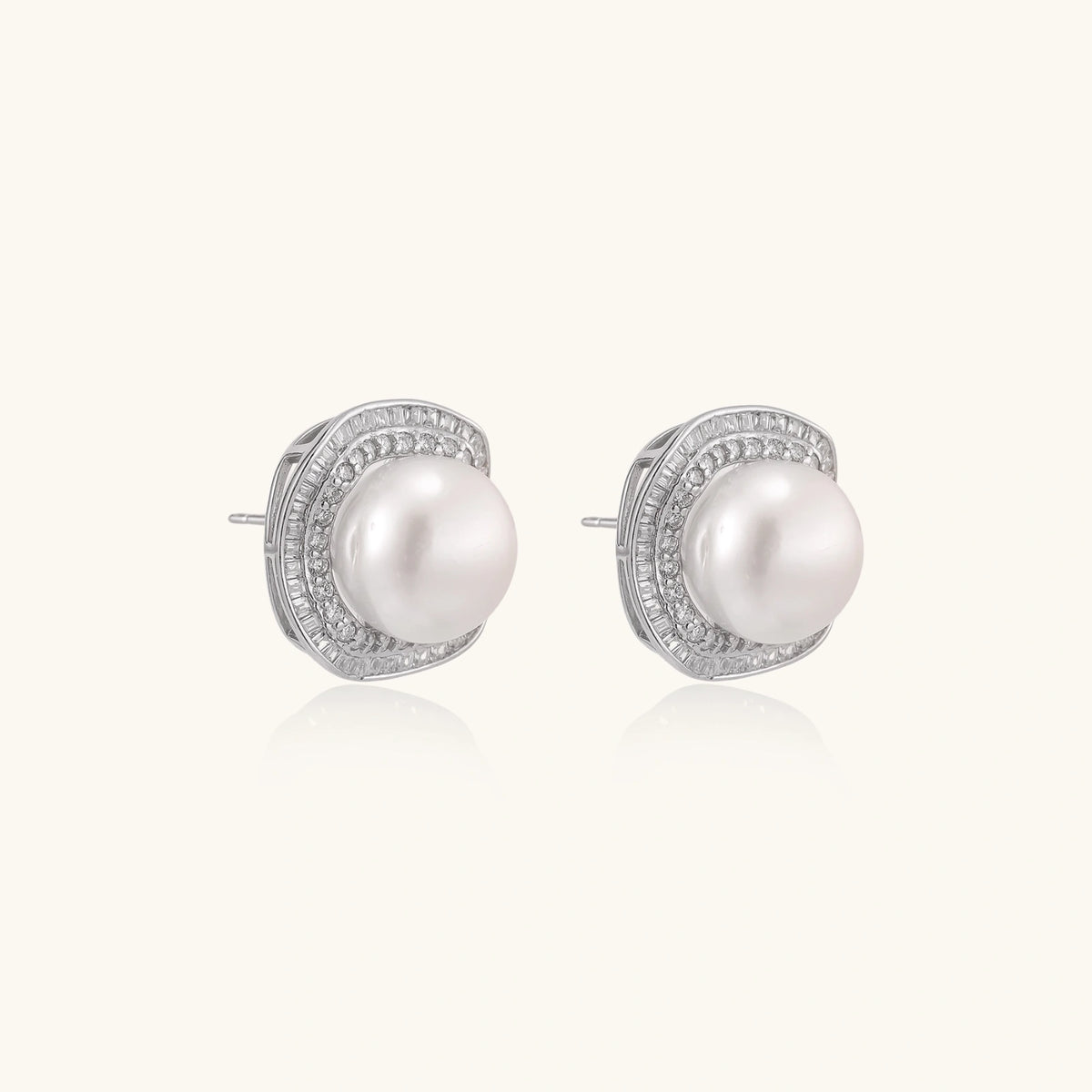 Rhodium-plated sterling silver stud earrings with round freshwater pearls surrounded by geometric crystal halos on cream background.